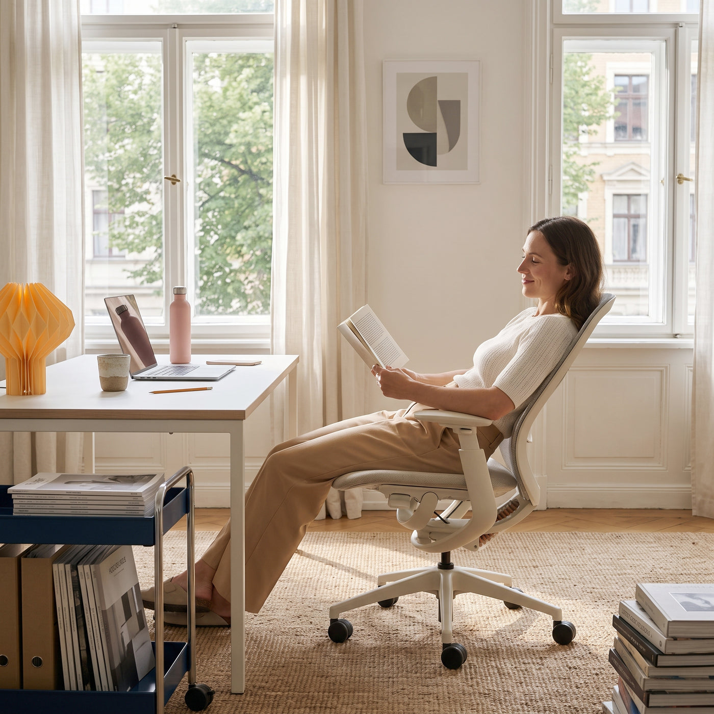 Woman reclining in a beige O2 ergonomic chair while reading beside a home office desk
